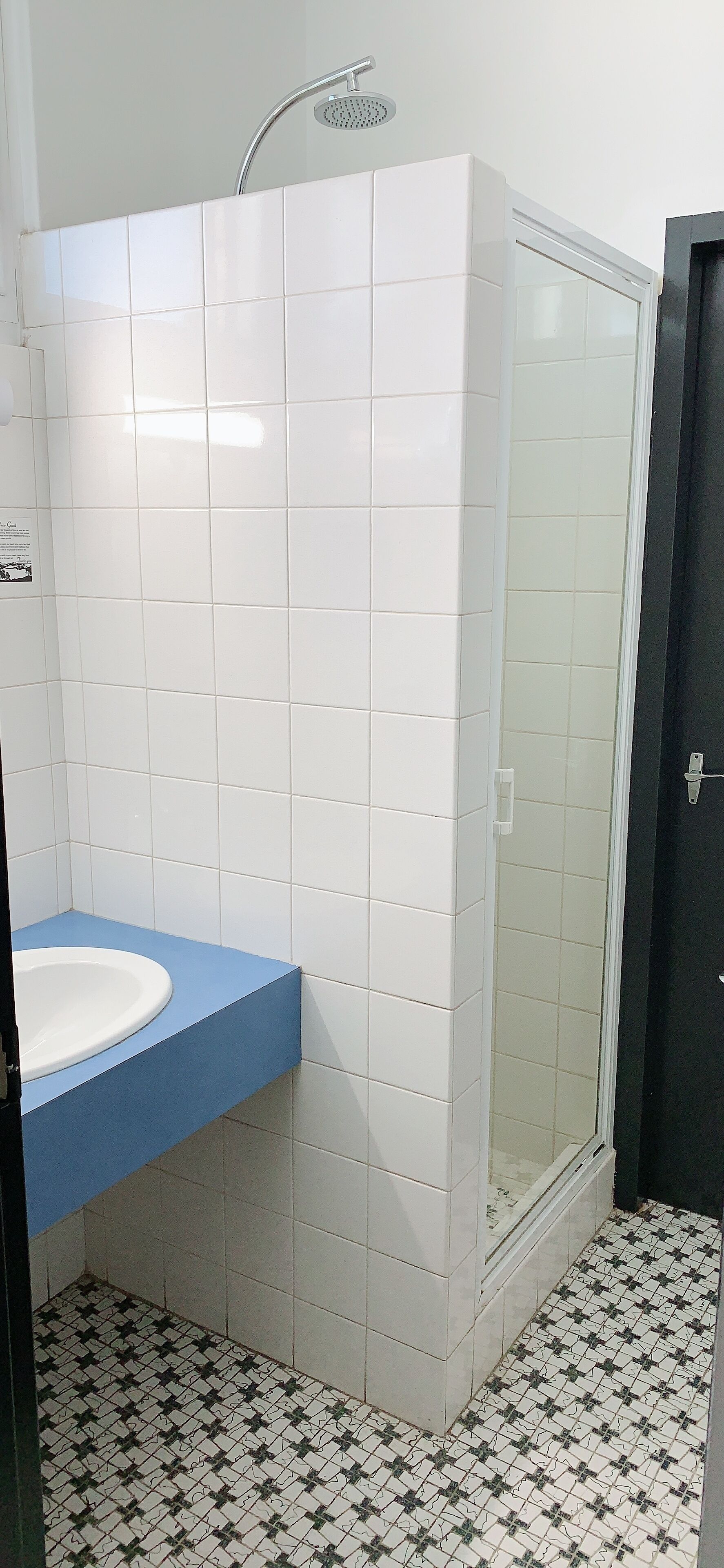 Un bany amb rajoles blanques, un lavabo blau i una dutxa amb envàs de vidre.