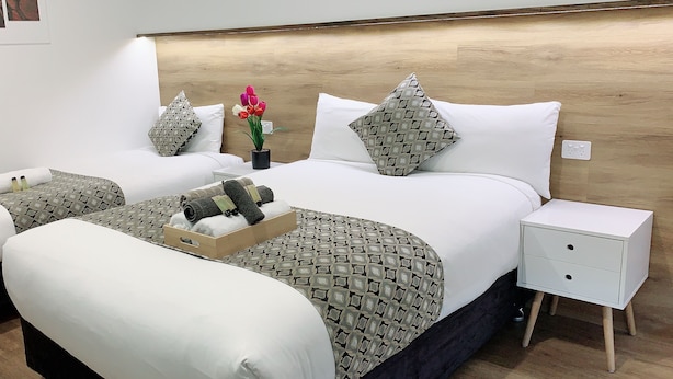 A hotel room with two beds, a wooden headboard, a nightstand with drawers, and a tray with towels and toiletries. - Elm Motel (Golden Square)