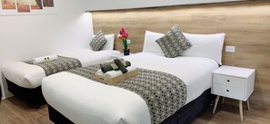 Une chambre d’hôtel avec deux lits, une tête de lit en bois, une table de chevet avec des tiroirs et un plateau avec des serviettes et des articles de toilette.