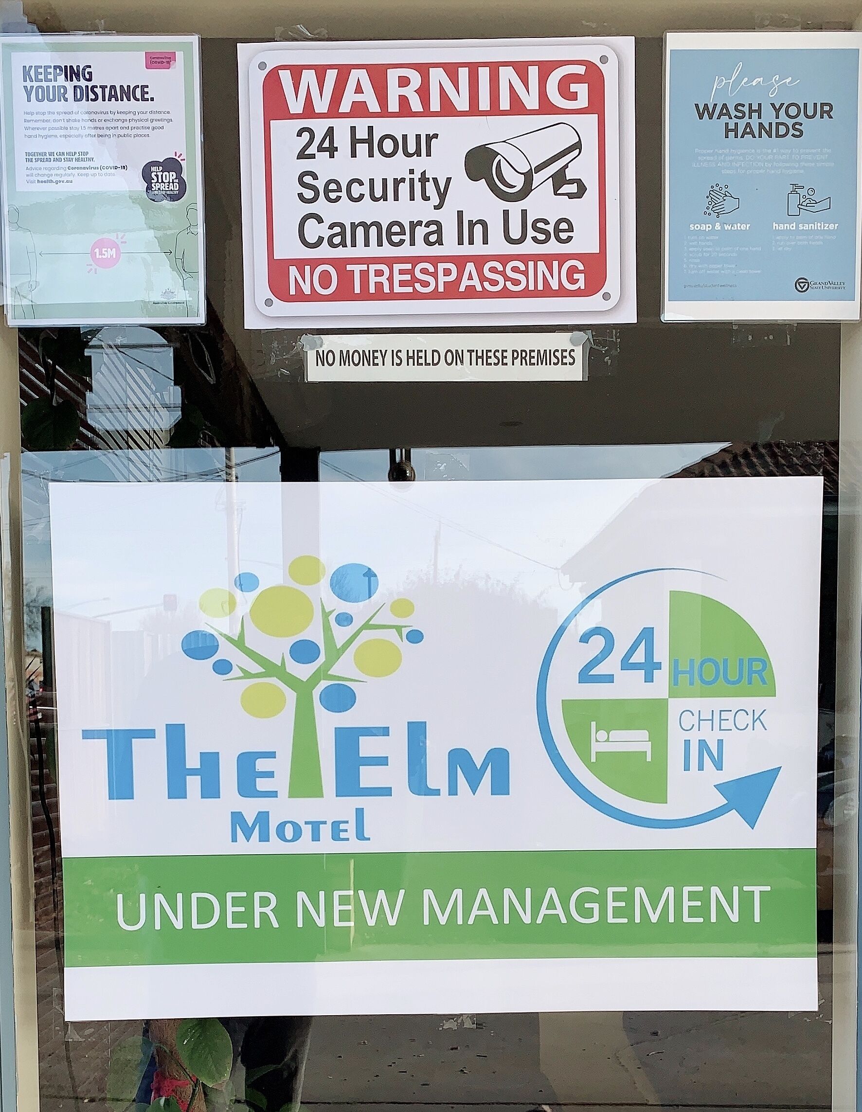 A motel sign with a 24-hour check-in policy and a warning about a security camera.