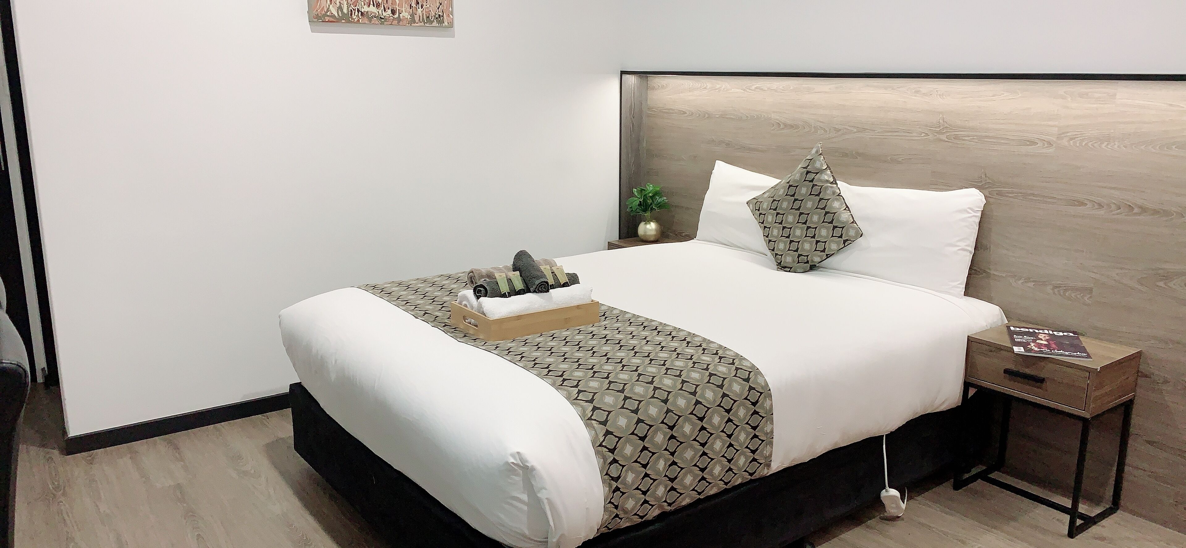 A neatly made bed with a patterned bedspread, a wooden headboard, and a bedside table with a book.