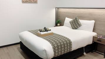 A neatly made bed with a patterned bedspread, a wooden headboard, and a bedside table with a book.