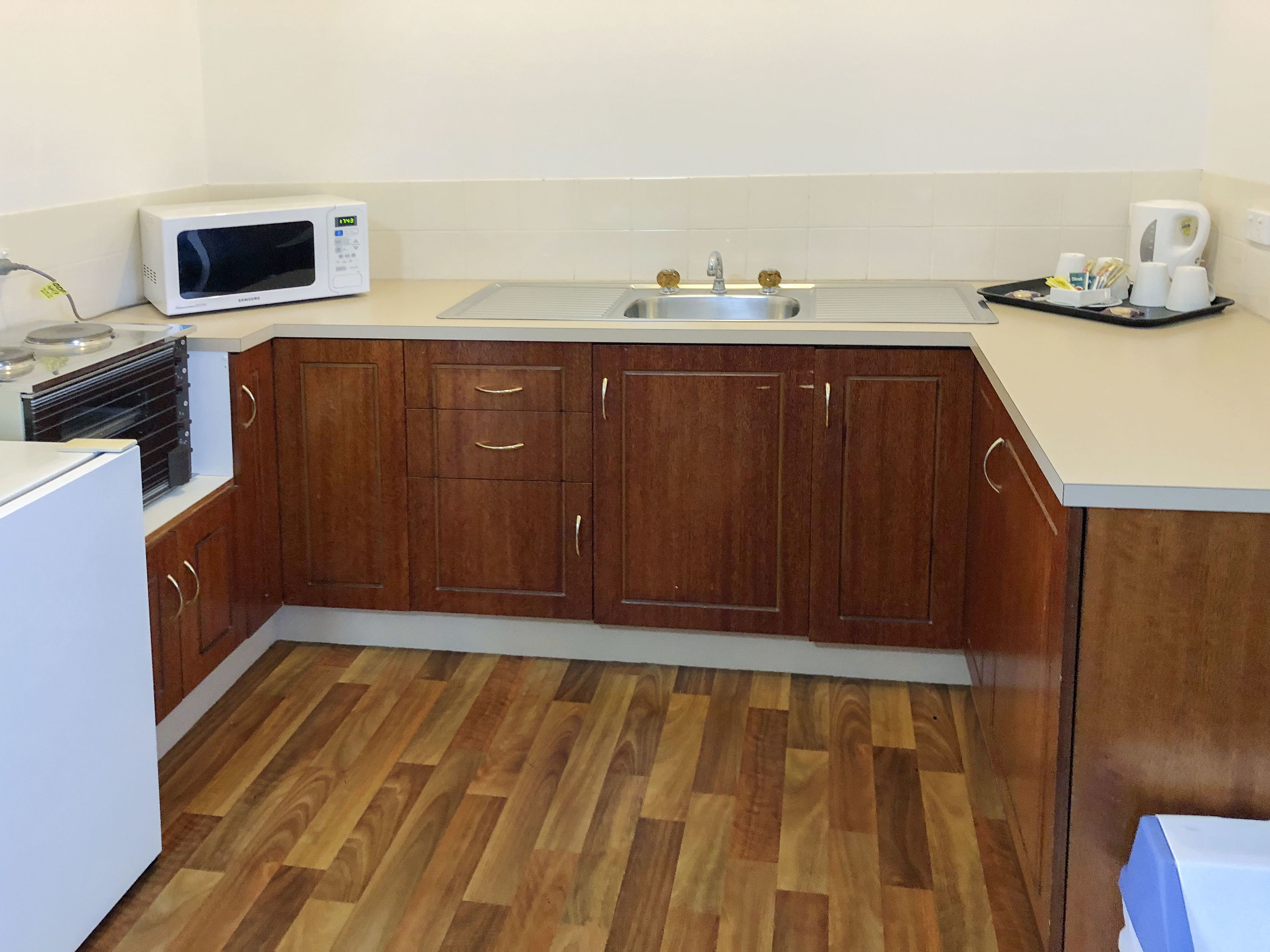 A compact kitchen with wooden cabinets, a microwave, a sink, and a coffee maker.