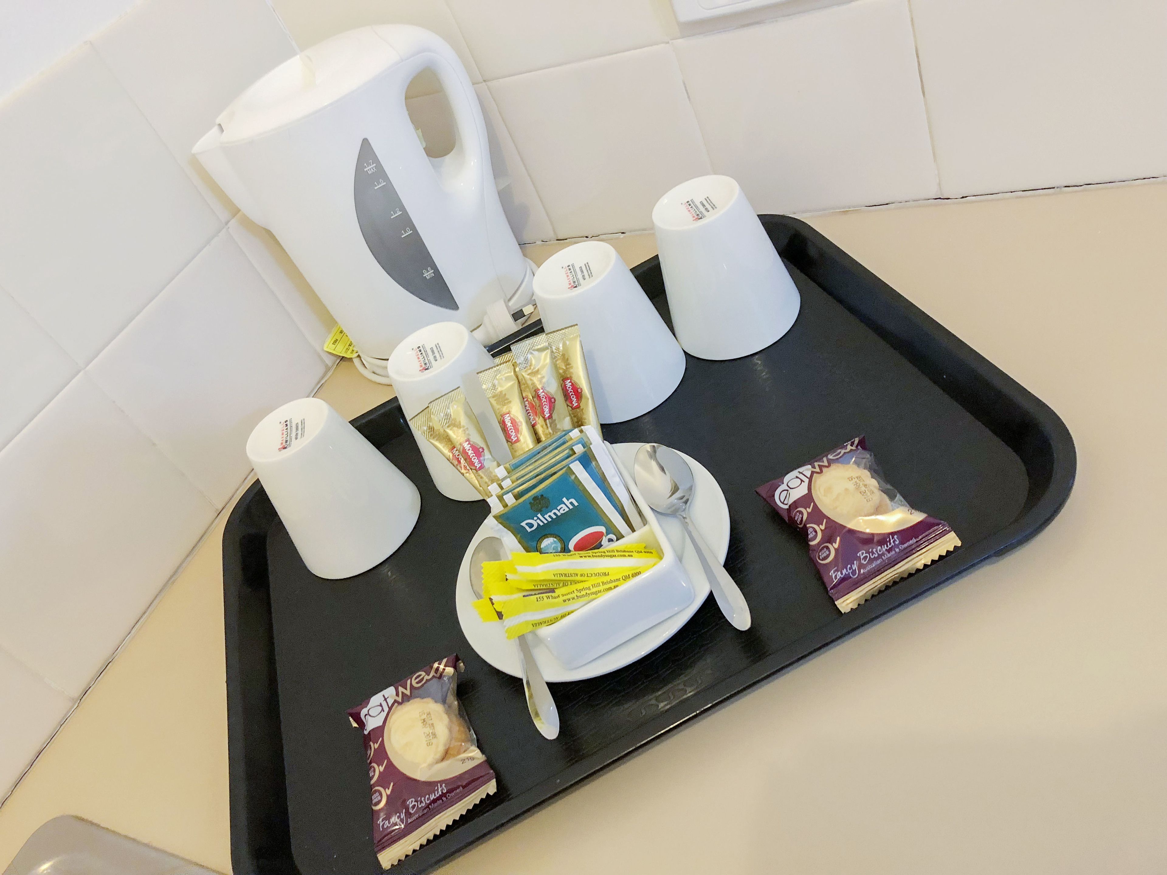 A tray with a coffee maker, cups, a plate with biscuits, and a packet of tea.