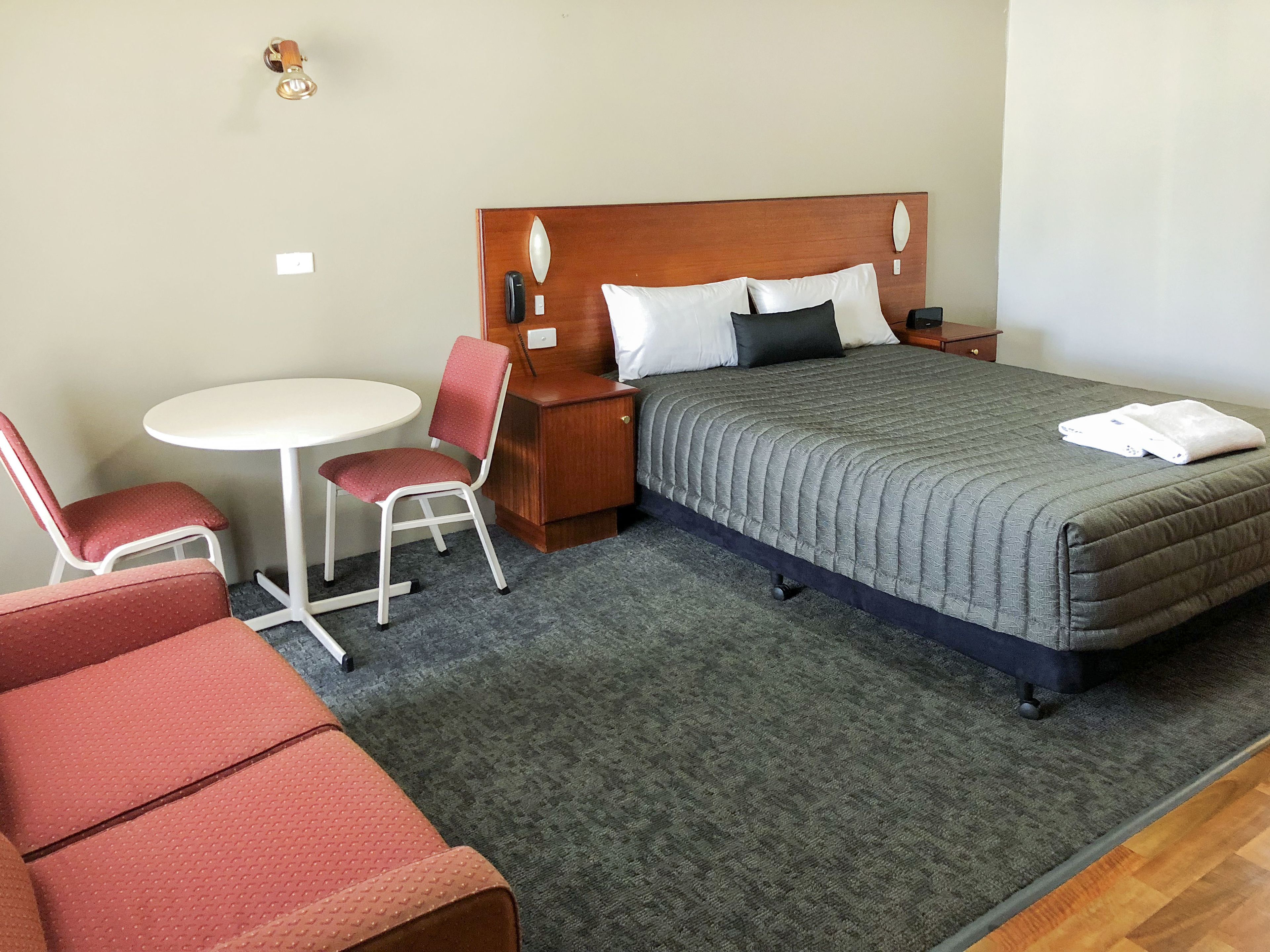 A hotel room with a bed, a small table, two chairs, a nightstand, and a telephone.