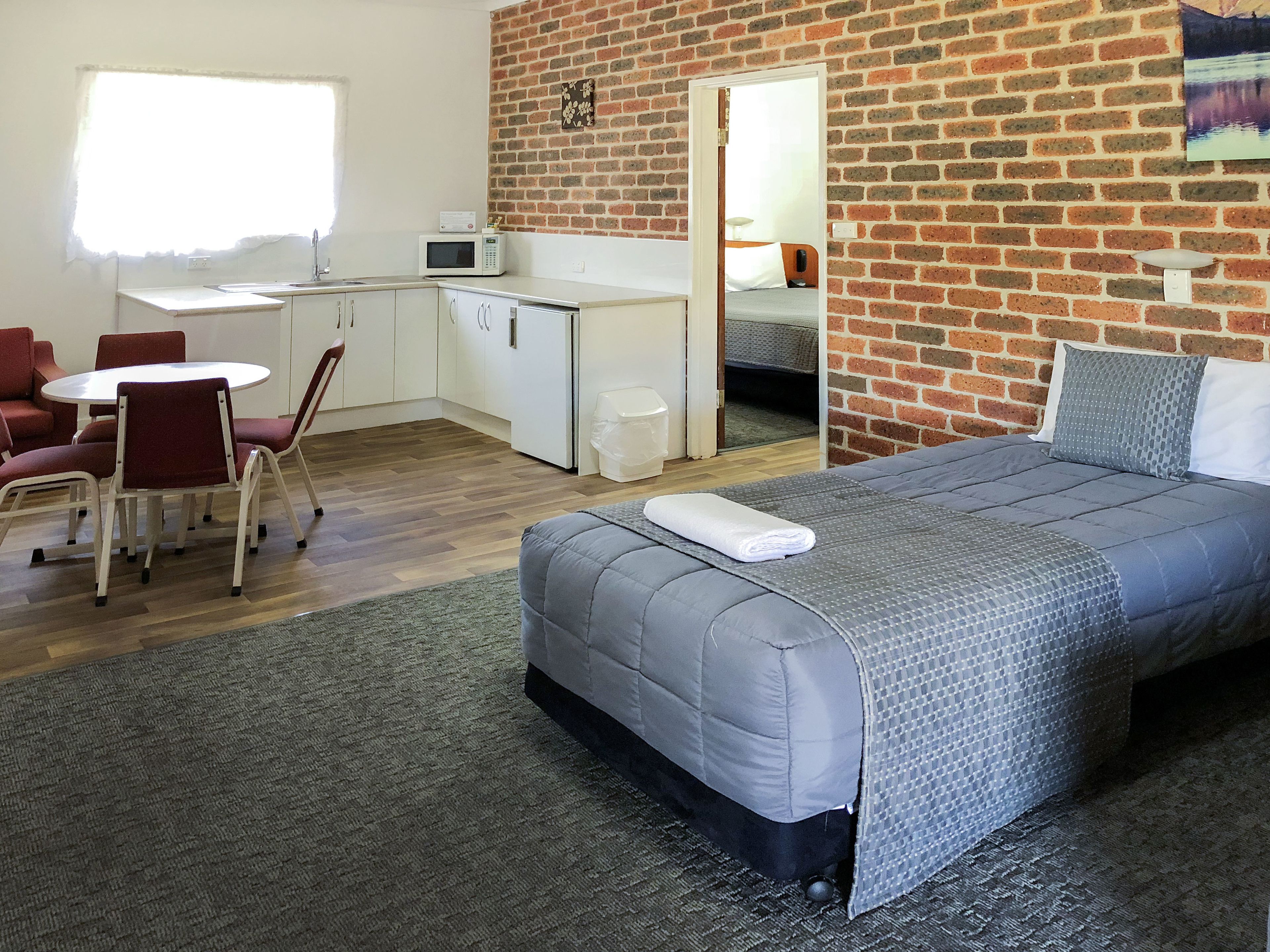 A compact hotel room with a bed, a small kitchenette, a dining area, and a bathroom.