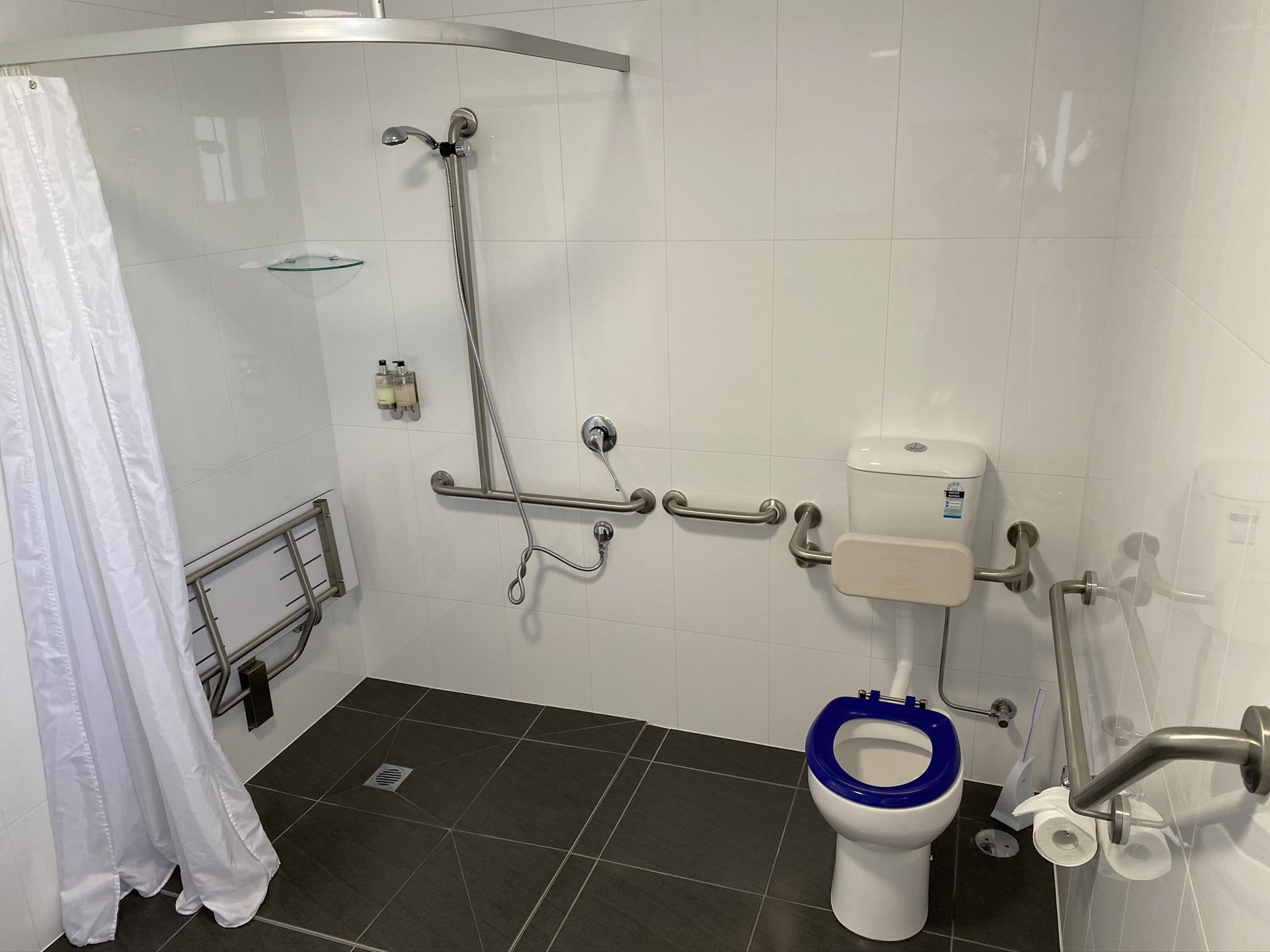 A bathroom with a shower, grab bars, a toilet with a blue seat, and a glass shower enclosure.