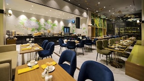 A modern dining area with multiple tables and chairs, a bar area, and a mural with tropical birds and plants. - Aviary Bintaro (South Tangerang)