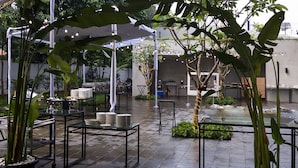 An outdoor dining area with tables and chairs, surrounded by greenery and a water feature. - Aviary Bintaro (South Tangerang)