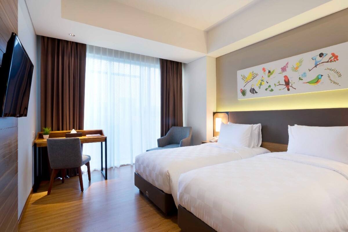 A hotel room with two beds, a desk, a chair, and a television.