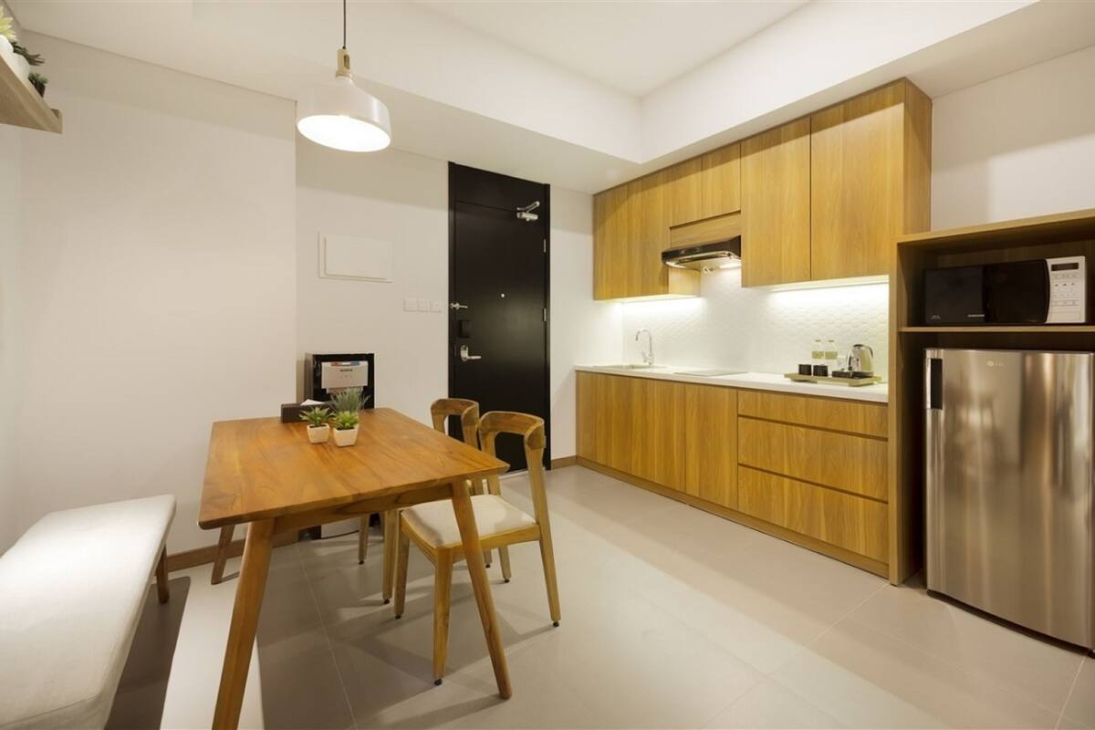 A modern kitchen with wooden cabinets, a stainless steel refrigerator, and a dining area with a wooden table and chairs.
