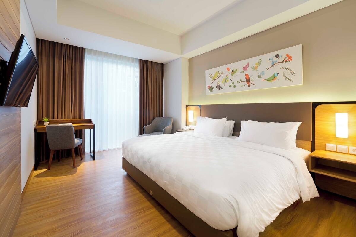 A hotel room with a large bed, a desk with a chair, a television, and a wall-mounted artwork.