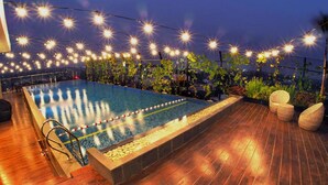 A rooftop pool with string lights, wooden deck, and lounge chairs. - Aviary Bintaro (South Tangerang)