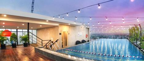Una piscina interior con vistas a la ciudad, rodeada de suelo de madera y plantas en macetas.