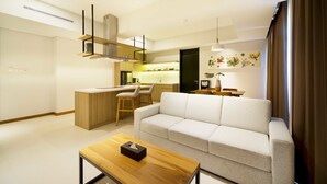 A modern living room with a sofa, a wooden coffee table, and a kitchen area with a bar and seating. - Aviary Bintaro (South Tangerang)