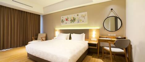 A hotel room with a large bed, a desk with a chair, a round mirror, and a wall-mounted artwork.