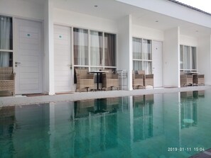 A poolside area with wicker chairs and tables, a clear pool, and a white building with large windows. - Villa Phyphy 2 (Gili Trawangan)