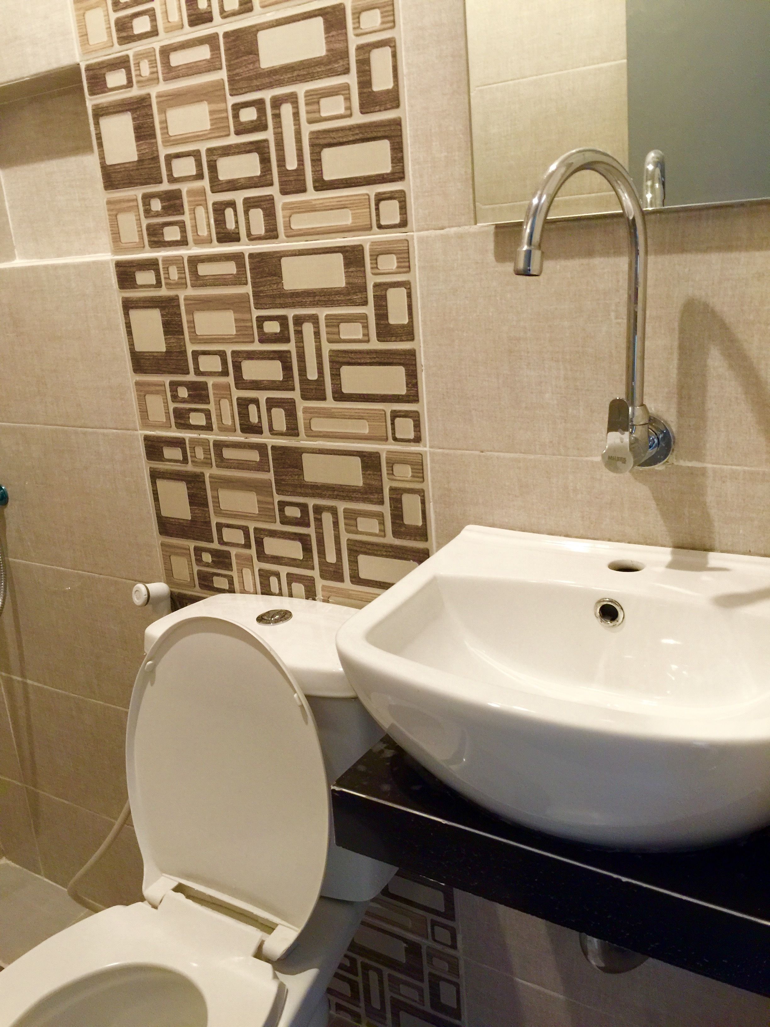 Un baño con inodoro, lavamanos y azulejos con diseño.