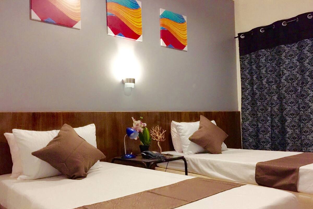A hotel room with two beds, a nightstand, a lamp, and a wall-mounted light.
