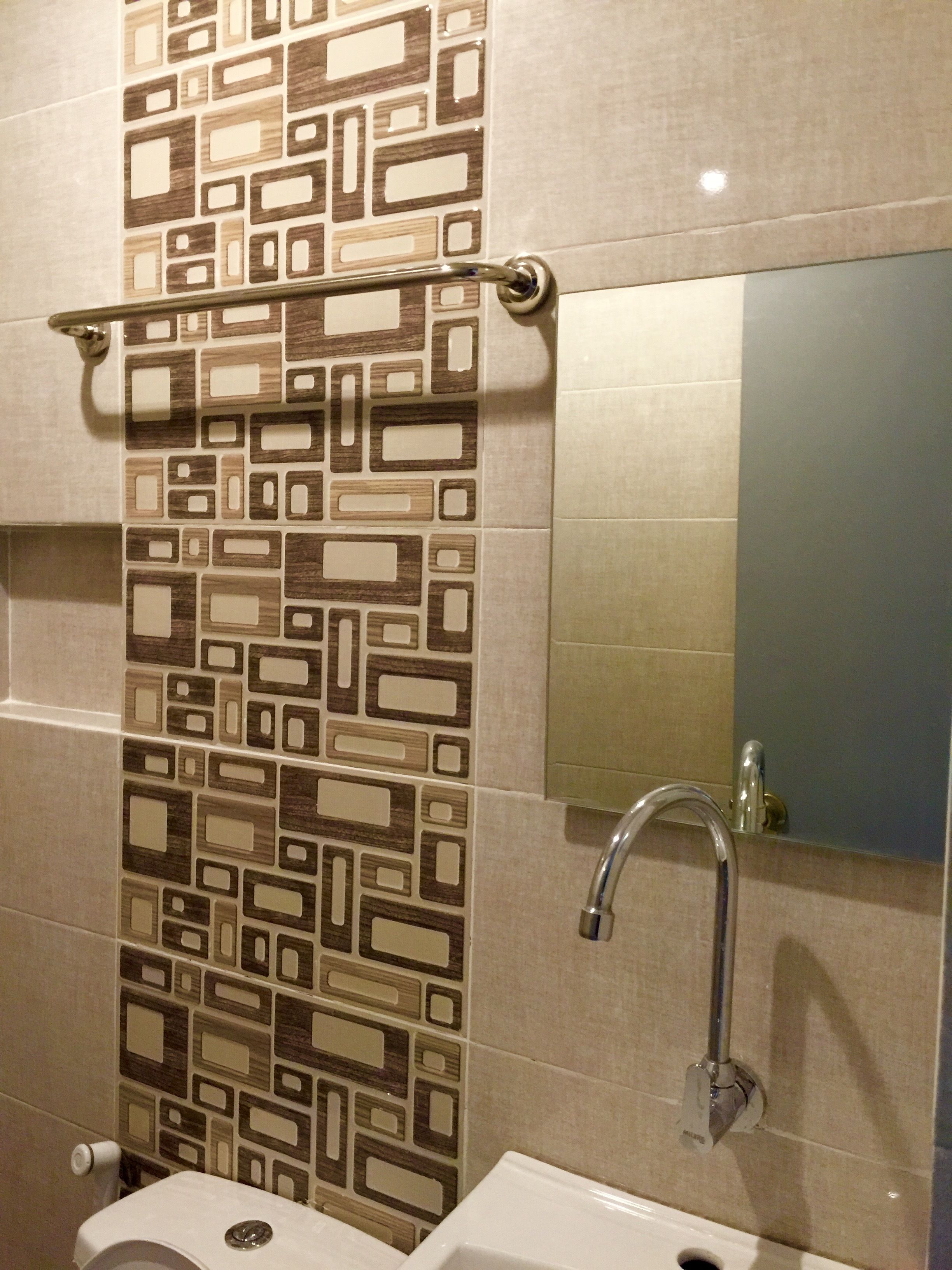 Un baño con pared de azulejos estampados, inodoro, lavamanos y espejo.