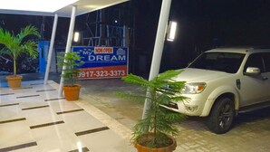 Entrada de un hotel con un letrero que dice 'ABIERTO' , un SUV estacionado y plantas en macetas.