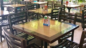 Un interior de restaurante con varias mesas y sillas, menús sobre las mesas y vistas al exterior a través de amplias ventanas.
