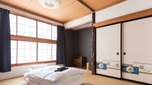 Una habitación japonesa tradicional con suelo de tatami, una cama con ropa de cama blanca, un futón, una puerta corredera con diseños decorativos y un mueble pequeño.
