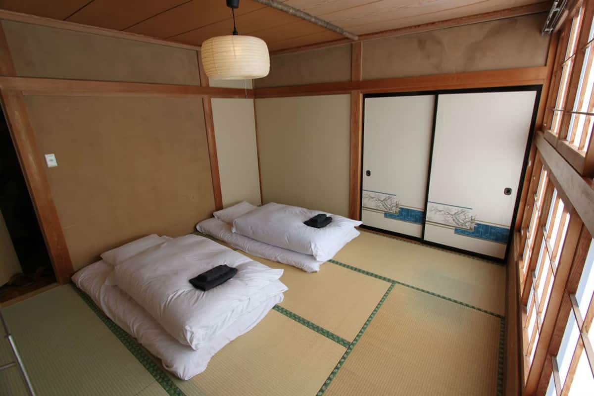A traditional Japanese room with tatami flooring, two beds with white bedding, a hanging paper lantern, and sliding doors with a blue and white design.
