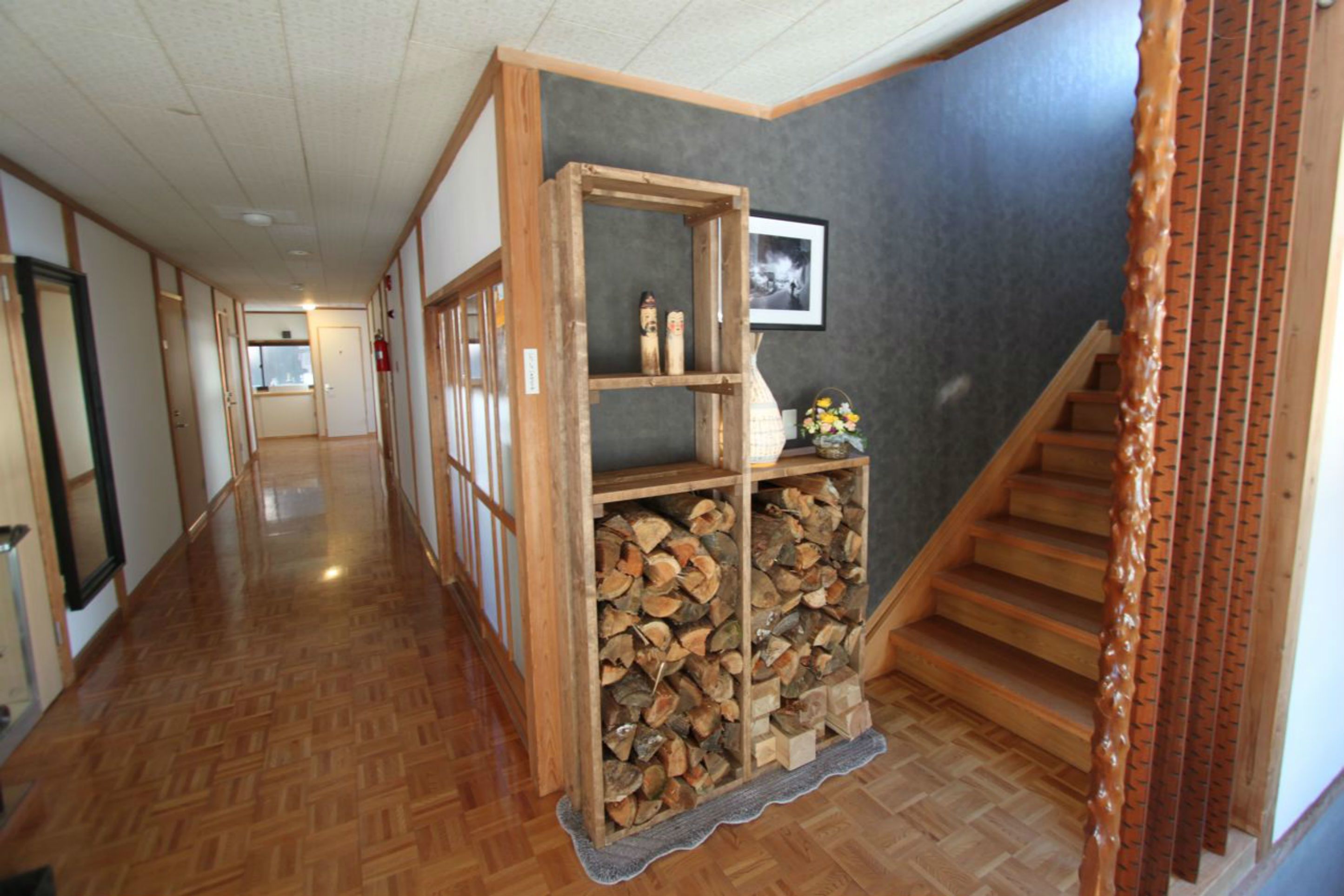A hallway with wooden flooring, a wooden display case with items, and a staircase.