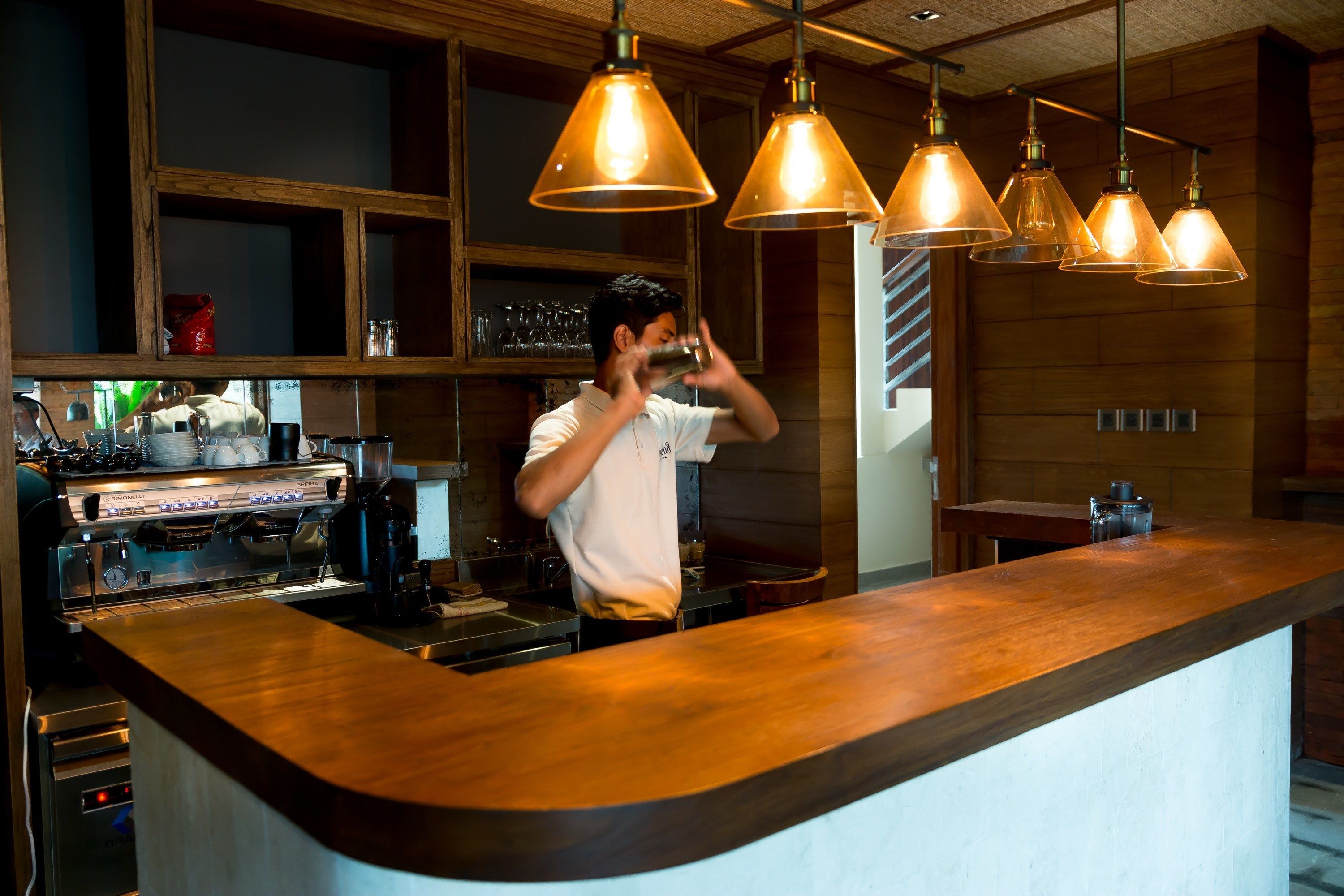 Eine Bar mit einer Holztresen, hängenden Pendelleuchten und einer Kaffeemaschine.