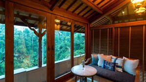 Un interior de madera con sofá y mesa, ventanas amplias con vistas a la vegetación.
