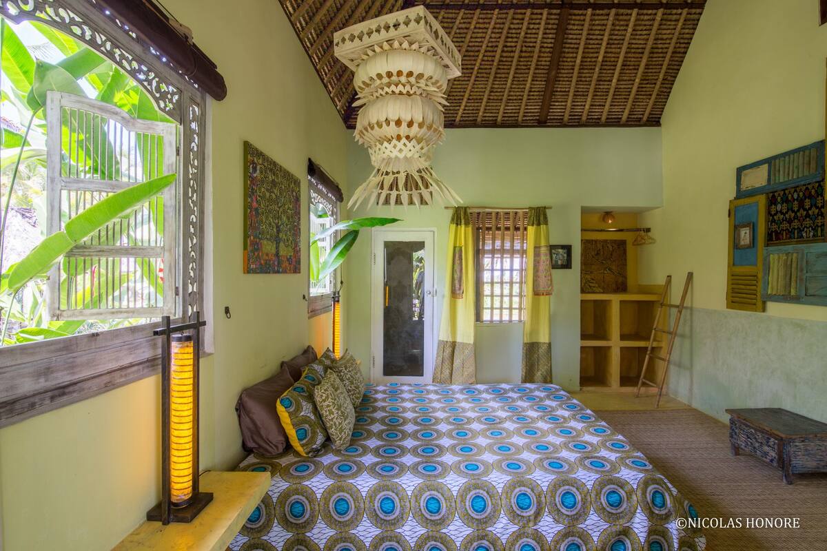 A room with a bed, a heater, a ladder, and a door leading to another room.