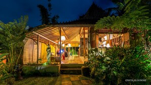 A traditional wooden building with a covered entrance, surrounded by lush greenery. - Hati Padi Cottages (Payangan)