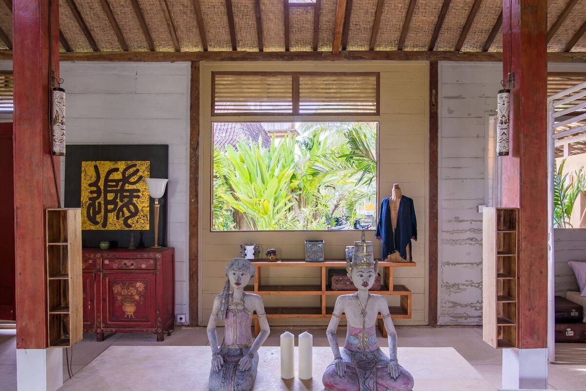 A room with a traditional thatched roof, a wooden cabinet with a floral design, a shelf with decorative items, and two statues.