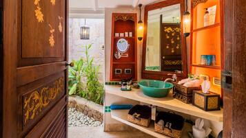 Un baño con puerta de madera, un espejo, un lavabo verde y repisas con artículos de aseo.
