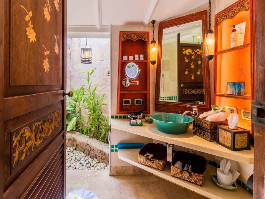 Un baño con puerta de madera, un espejo, un lavabo verde y repisas con artículos de aseo.