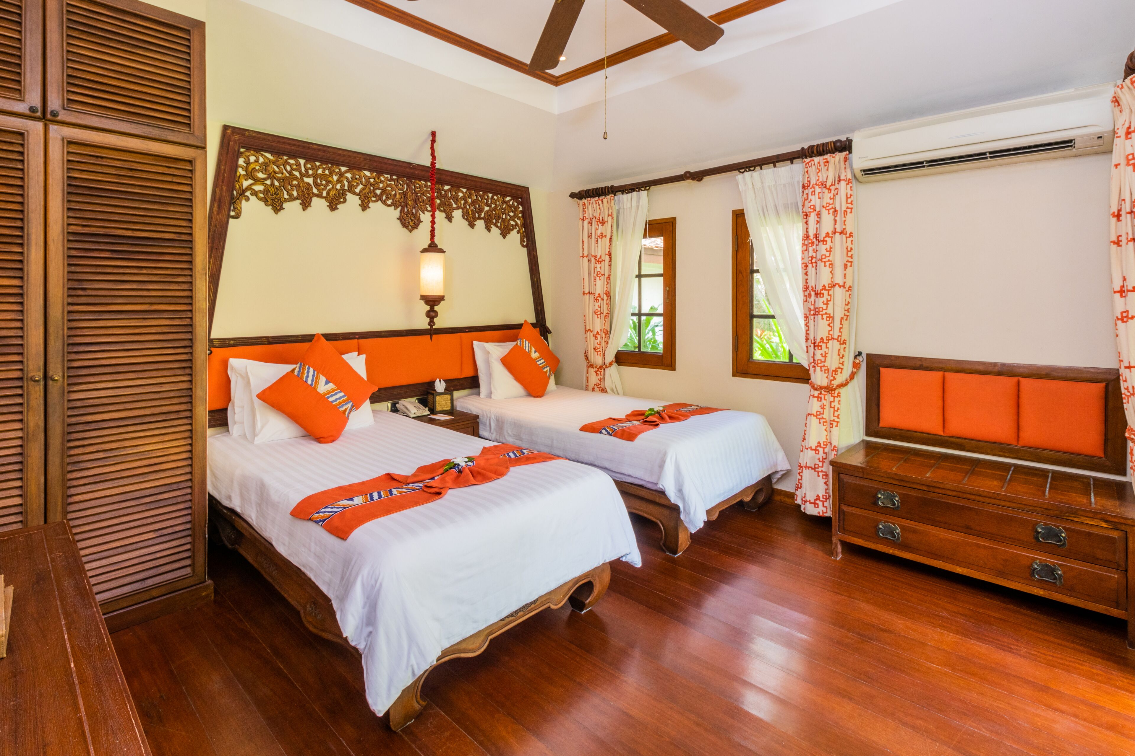 A hotel room with two beds, wooden flooring, a dresser, and a ceiling fan.