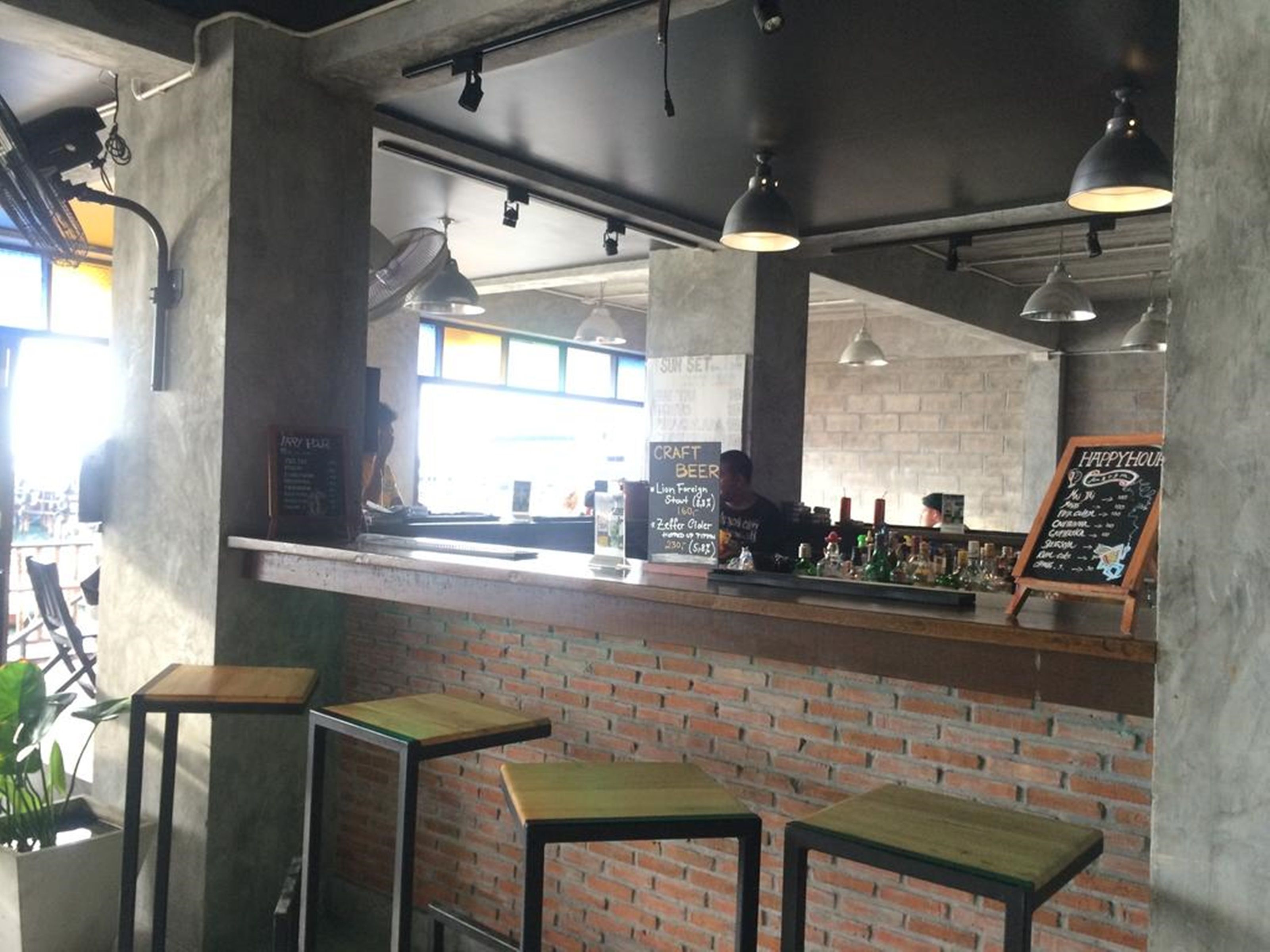 A bar area with brick walls, wooden stools, and a counter displaying various bottles.