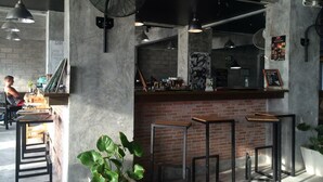 A bar area with a brick counter, metal stools, and a fan. - Bro&Sis Place (Koh Tao)