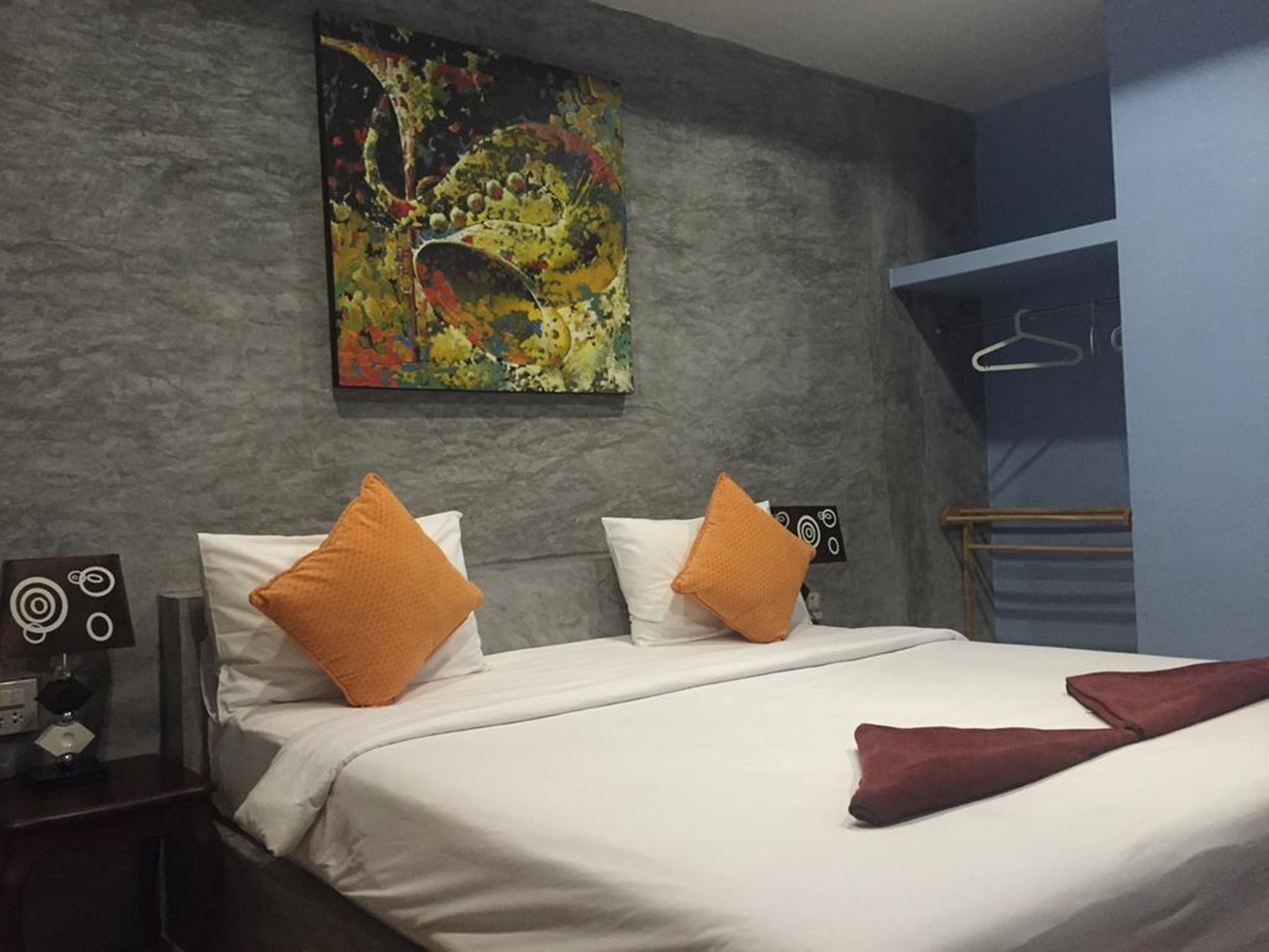 Una habitació d'hotel amb un llit, dos almoinos, un quadre a la paret, una taula de nit i una perxa per abrigalls.
