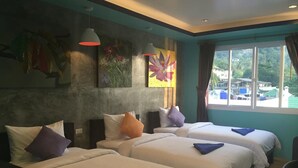 A hotel room with two beds, each with a blue pillow, a large window with a view of the outdoors, and artwork on the wall. - Bro&Sis Place (Koh Tao)
