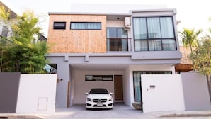 Una casa moderna de dos pisos con fachada blanca, sección de madera en el nivel superior y un coche blanco estacionado en la entrada.