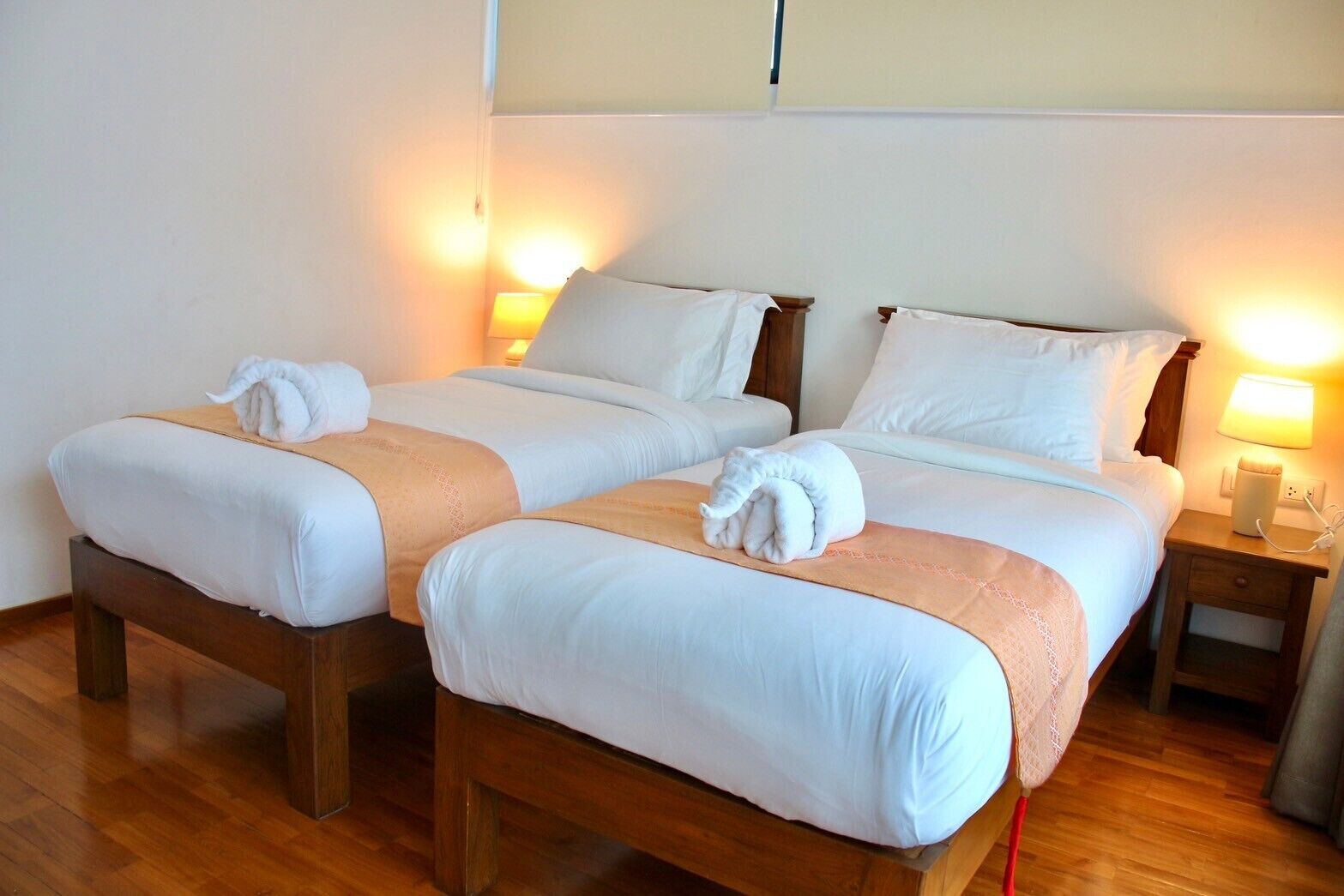 Habitación de hotel con dos camas individuales, cabeceros de madera, ropa de cama blanca y lámparas de noche.