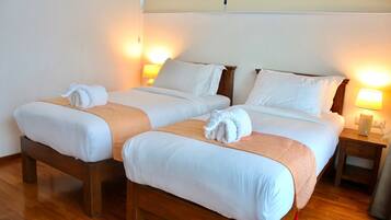Habitación de hotel con dos camas individuales, cabeceros de madera, ropa de cama blanca y lámparas de noche.