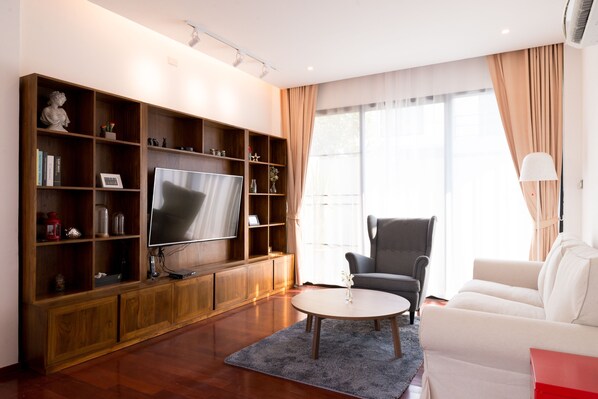 Una sala de estar moderna con televisor de pantalla plana, estanterías de madera, un sillón gris, un sofá blanco y una mesita auxiliar roja.