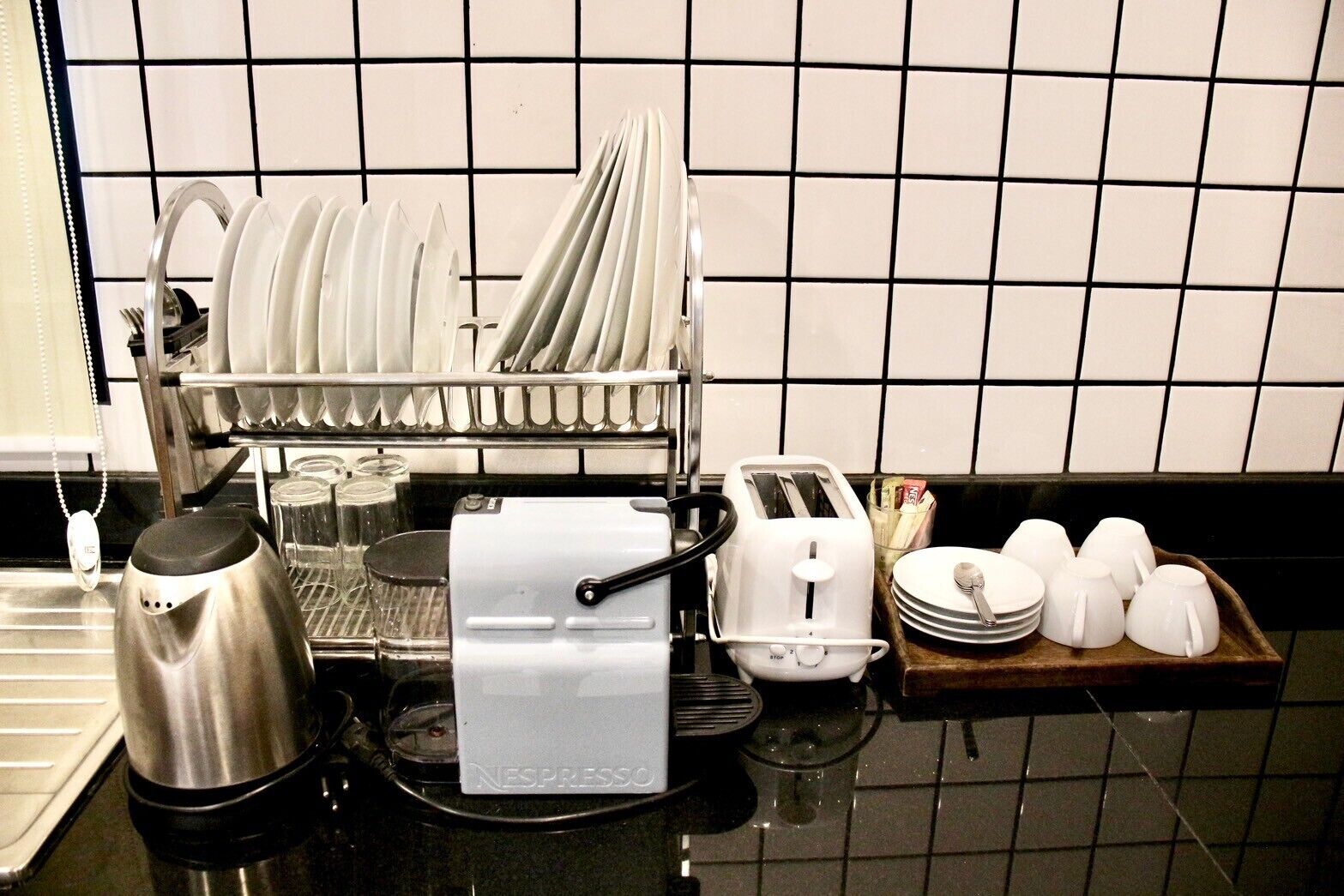 Una cocina con un escurreplatos, una cafetera, un tostador y una bandeja con tazas y platos.