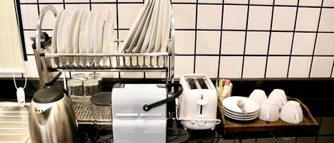 Una cocina con un escurreplatos, una cafetera, un tostador y una bandeja con tazas y platos.