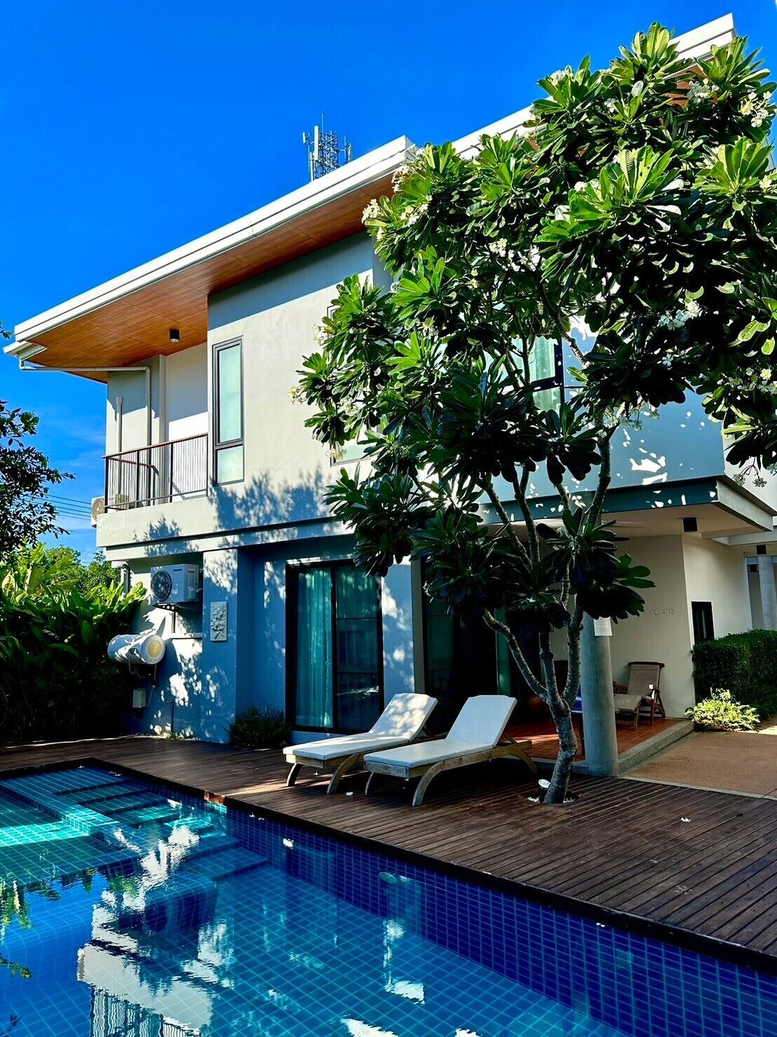 A modern two-story house with a swimming pool, a covered patio, and a large tree in the backyard.