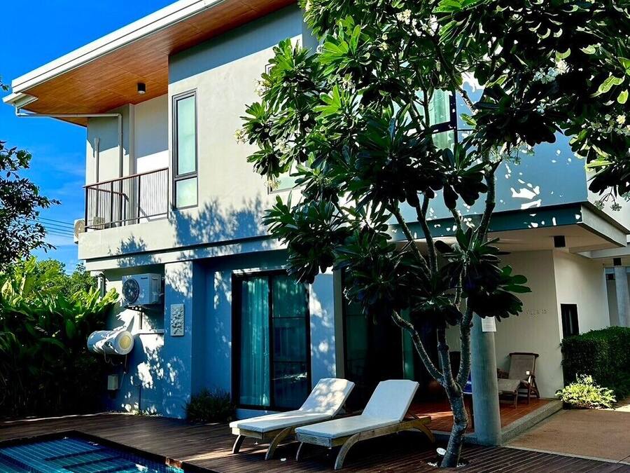 A modern two-story house with a swimming pool, a covered patio, and a large tree in the backyard.