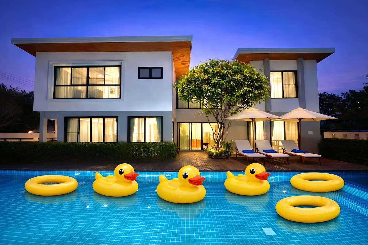 A modern two-story house with a swimming pool, inflatable ducks, and lounge chairs.